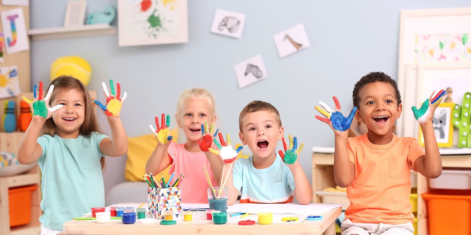 Four children holding up hands covered in bright finger paint at a craft table
