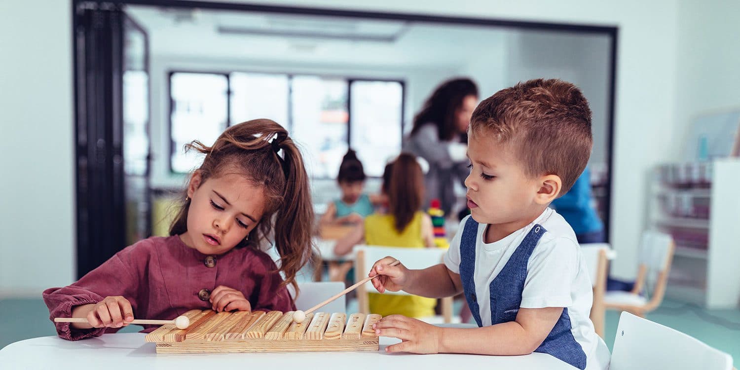 Two children playing a wooden xylophone together at a classroom table