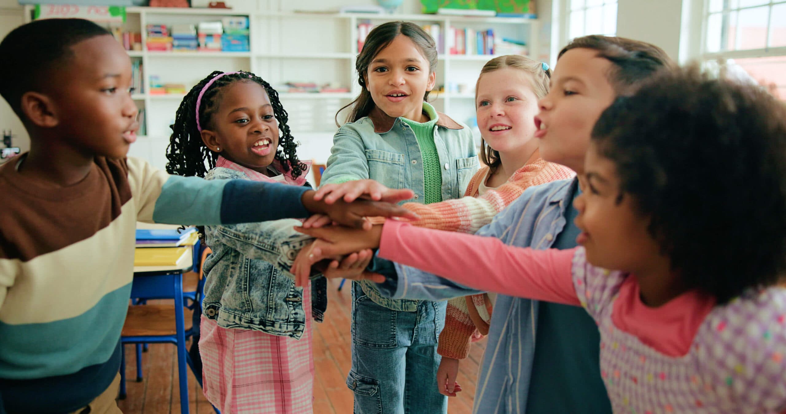 A circle of children stacking their hands together in the middle of the classroom