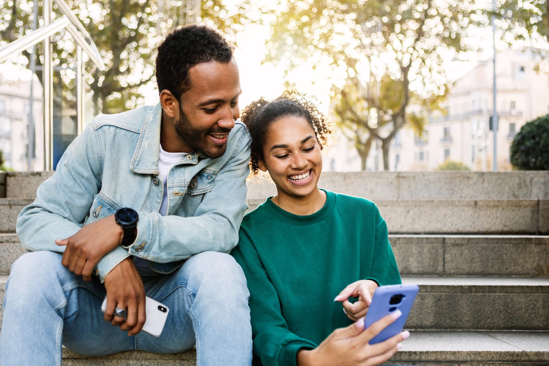 Two parents smiling at a phone together on a bench outdoors