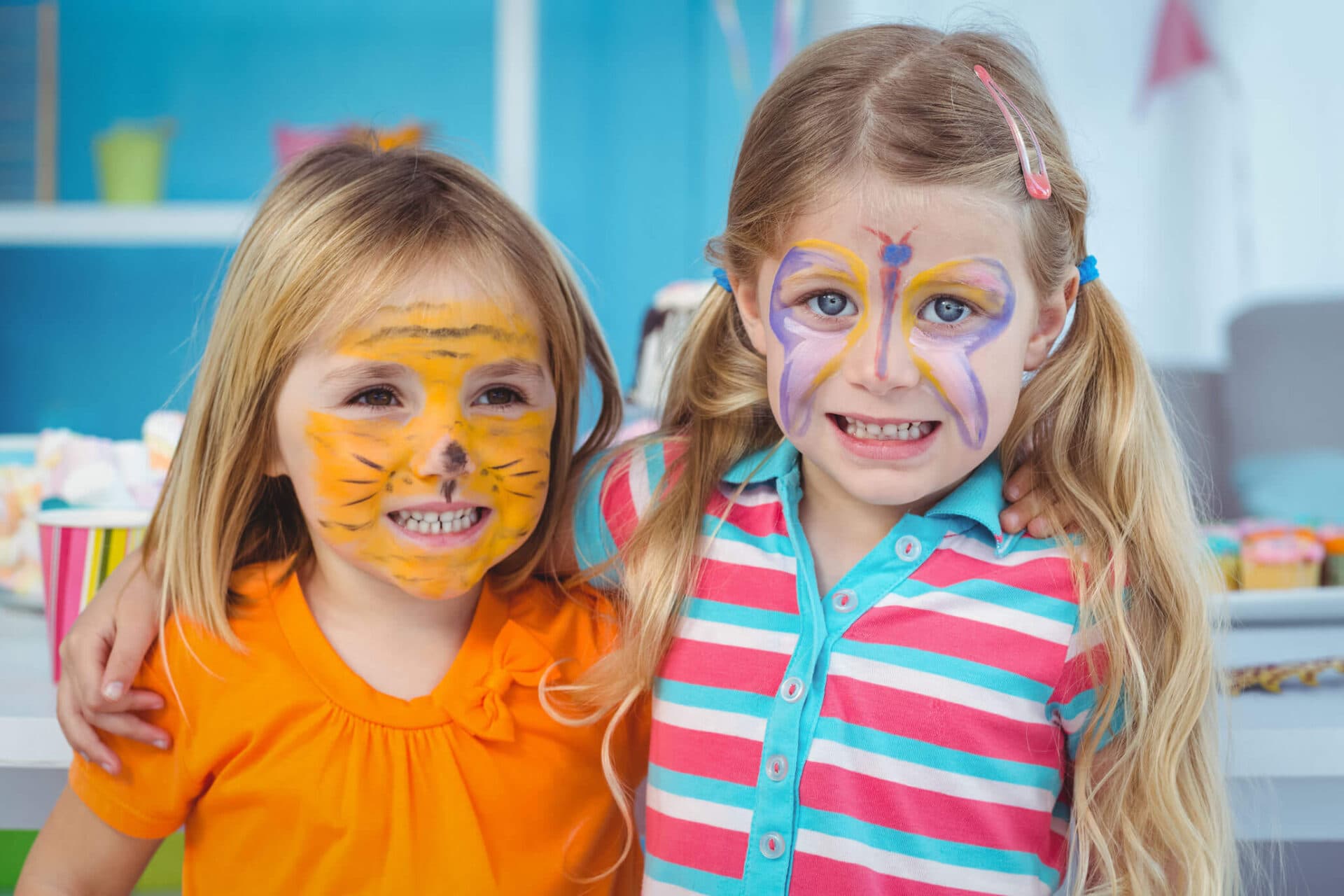 Two girls with tiger and butterfly face paint smiling at the camera