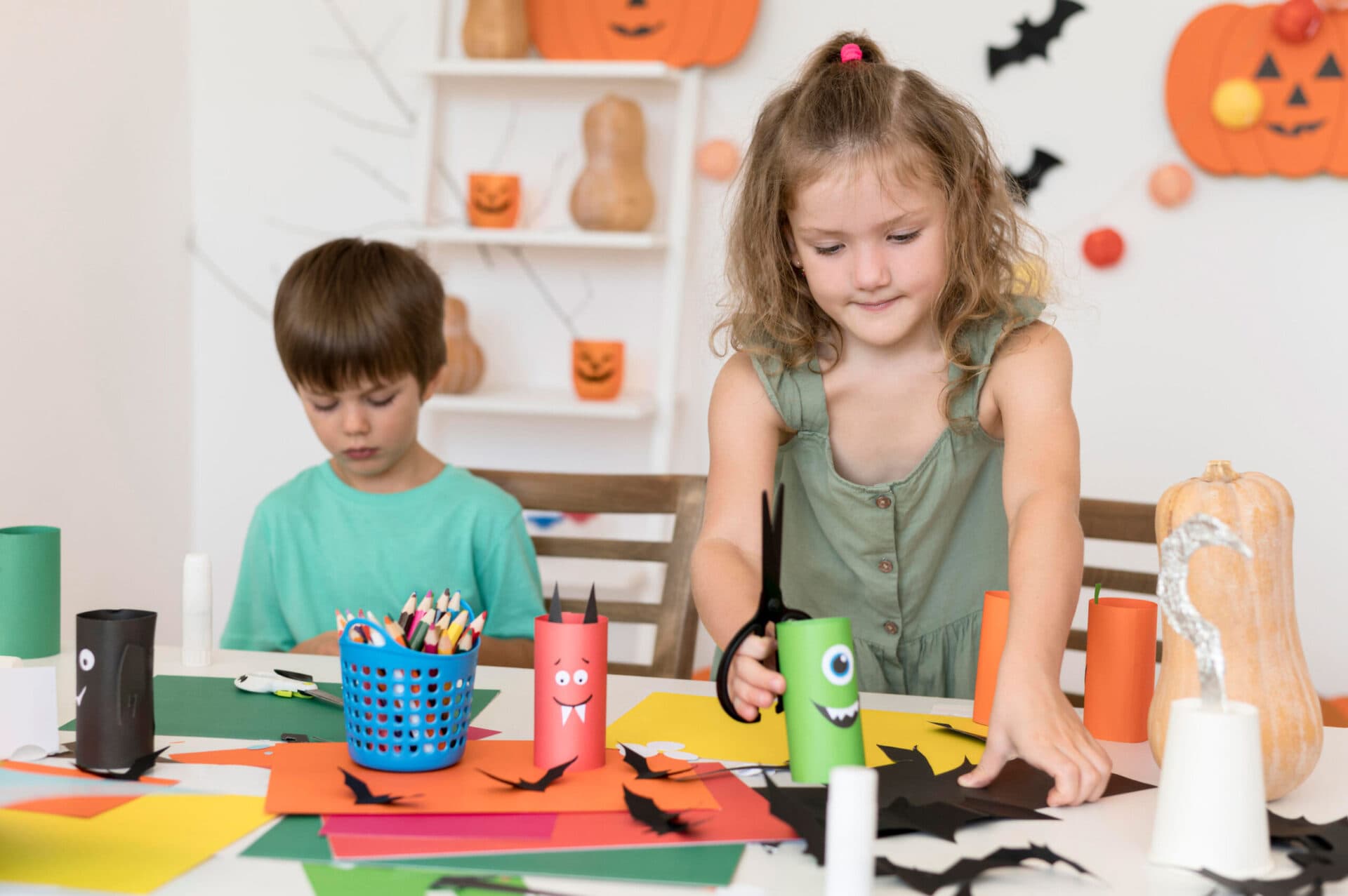 Two children making monster crafts from cardboard tubes at a decorated table