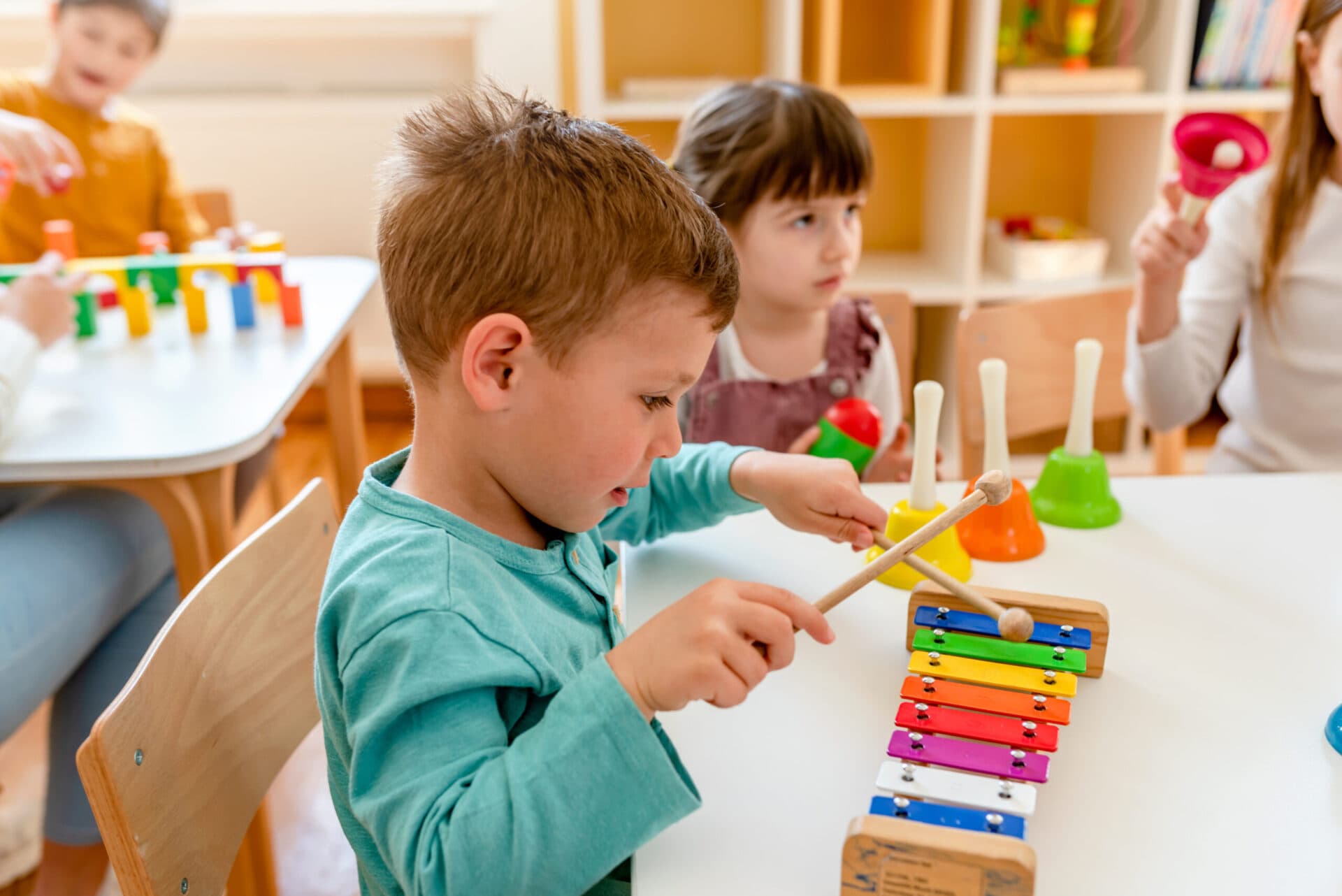 A boy playing a xylophone with a mallet while classmates look on