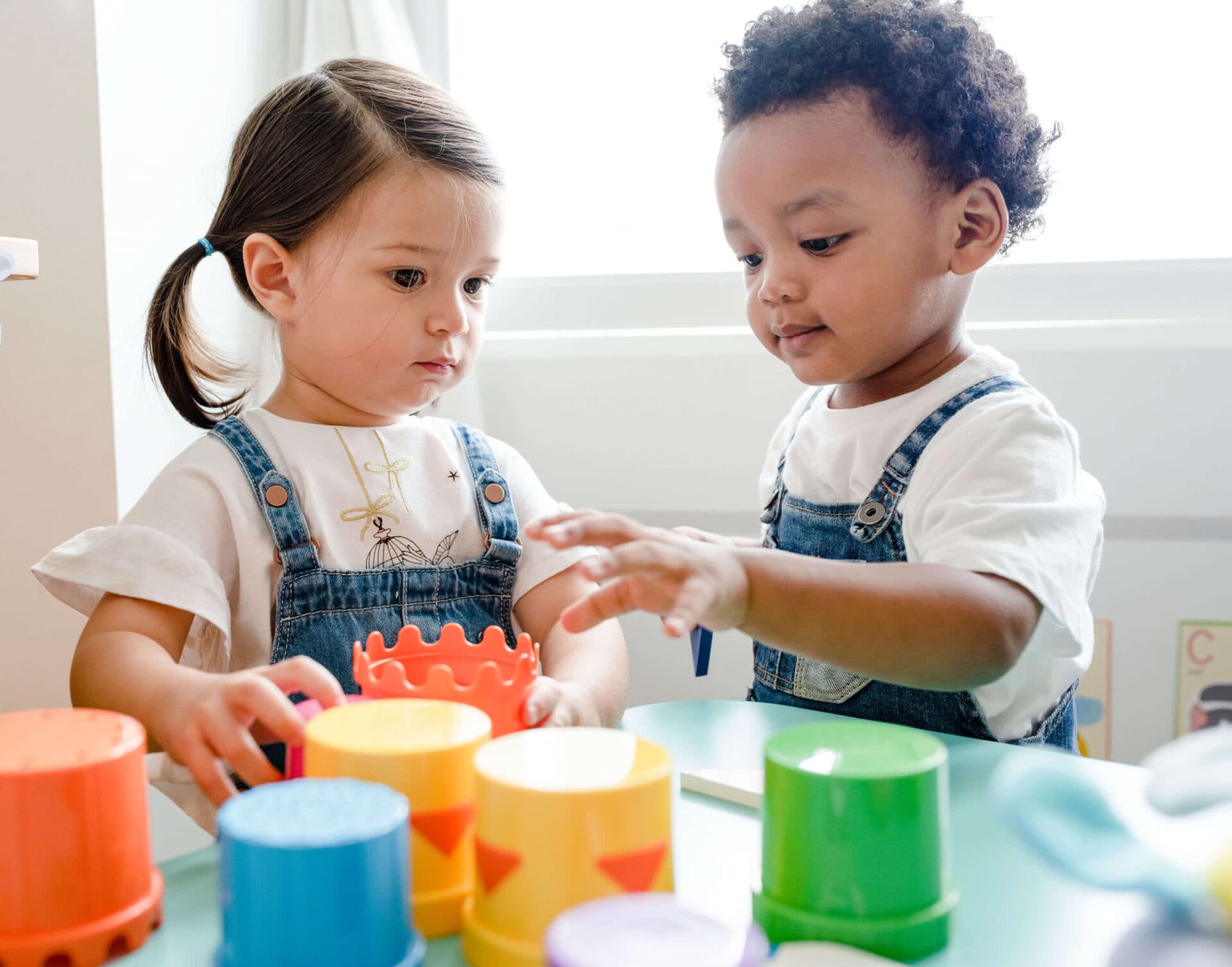 Two toddlers stacking bright plastic cups together at a low table