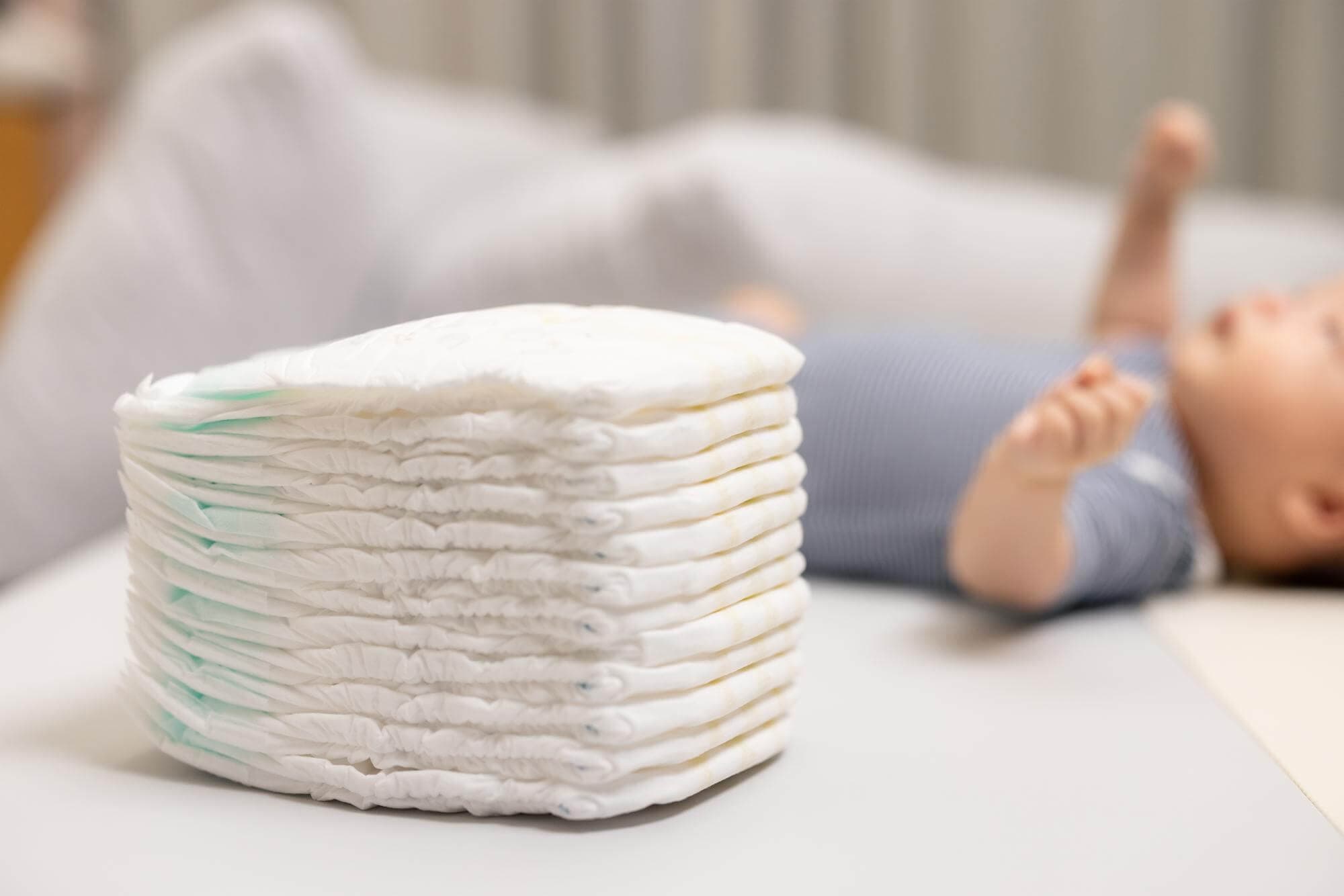 A neat stack of nappies beside a baby lying on a changing mat