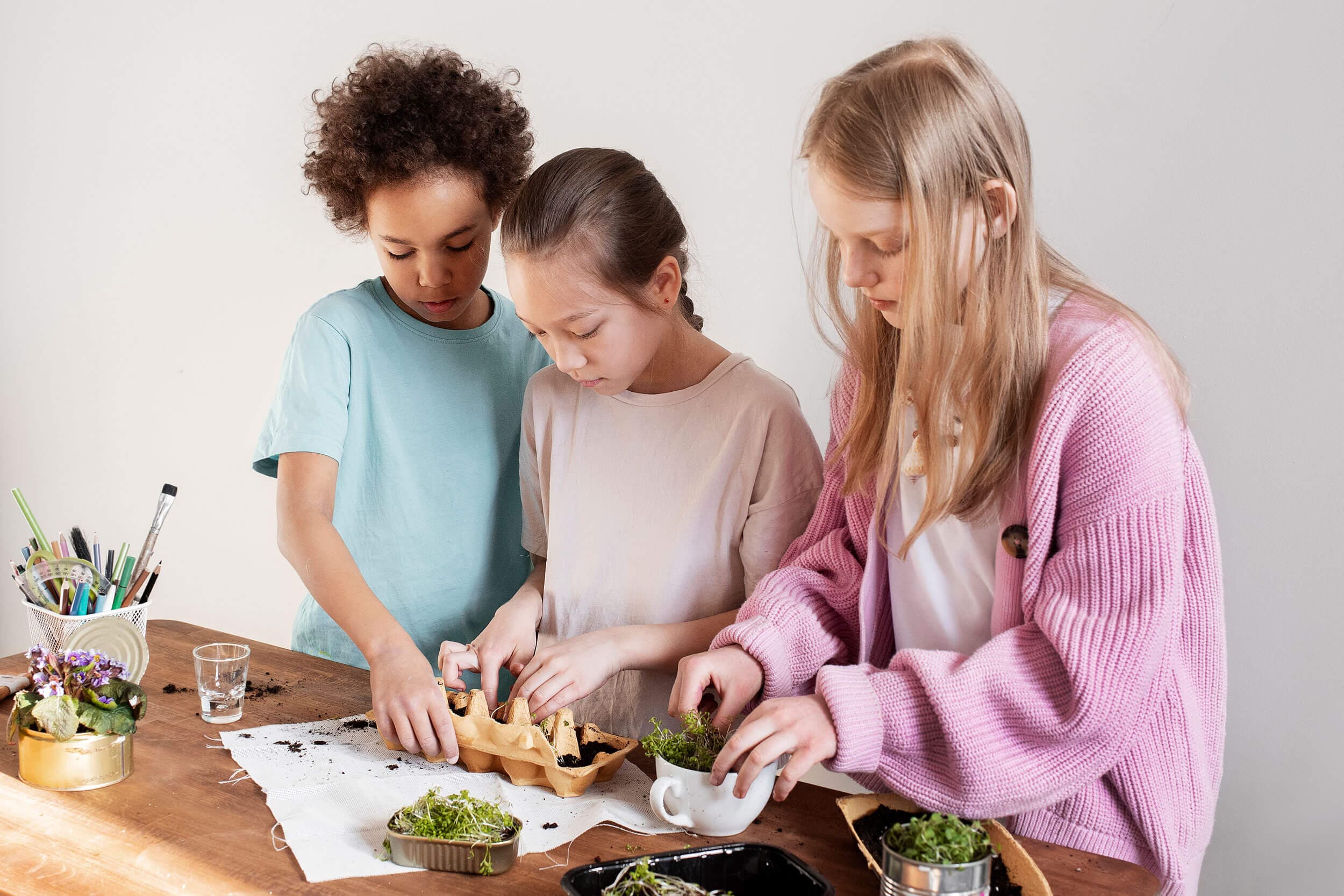 Three older children preparing food together at a kitchen worktop