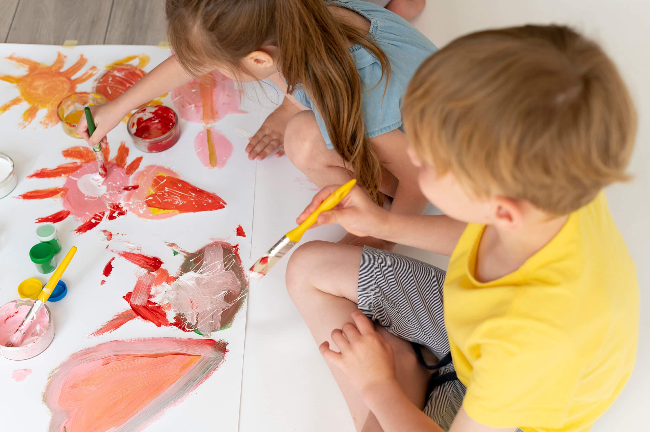 Two children finger-painting a bright red and orange picture on the floor
