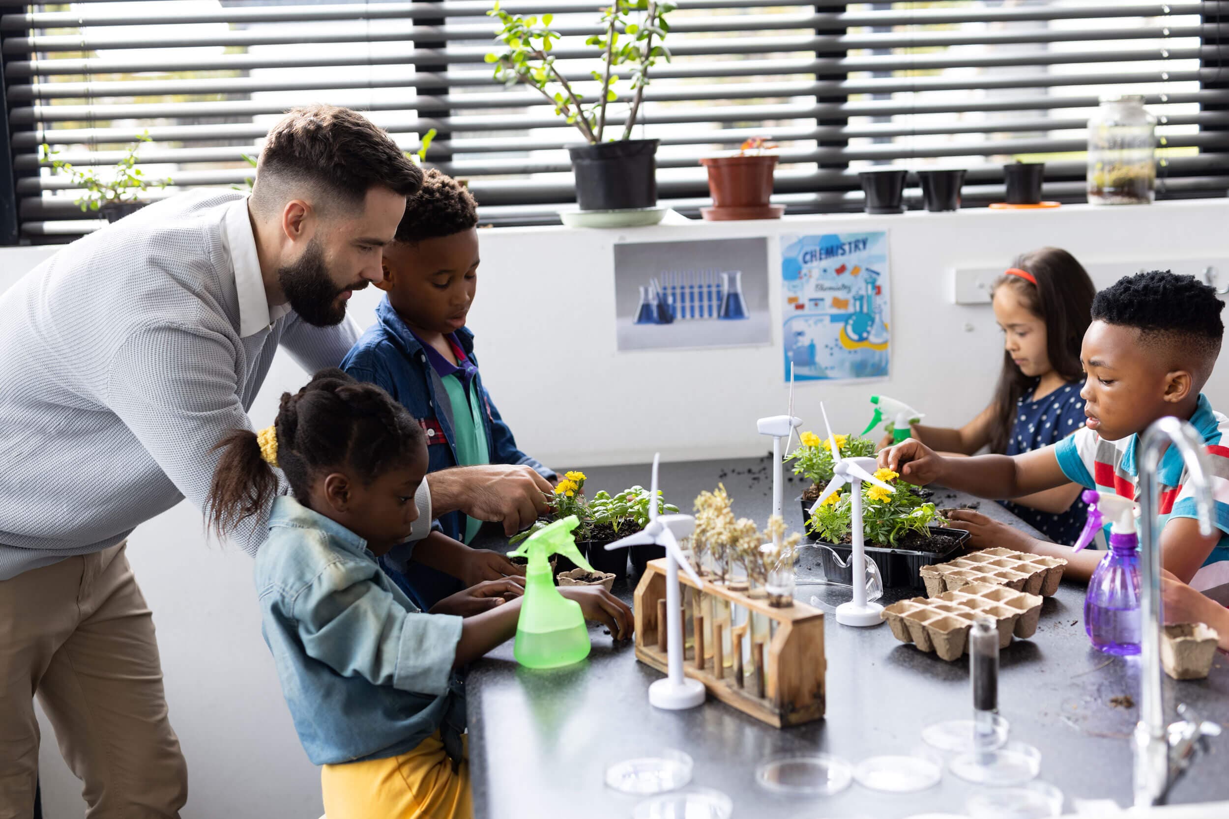A teacher and children tending plants and watering seedlings at a classroom bench