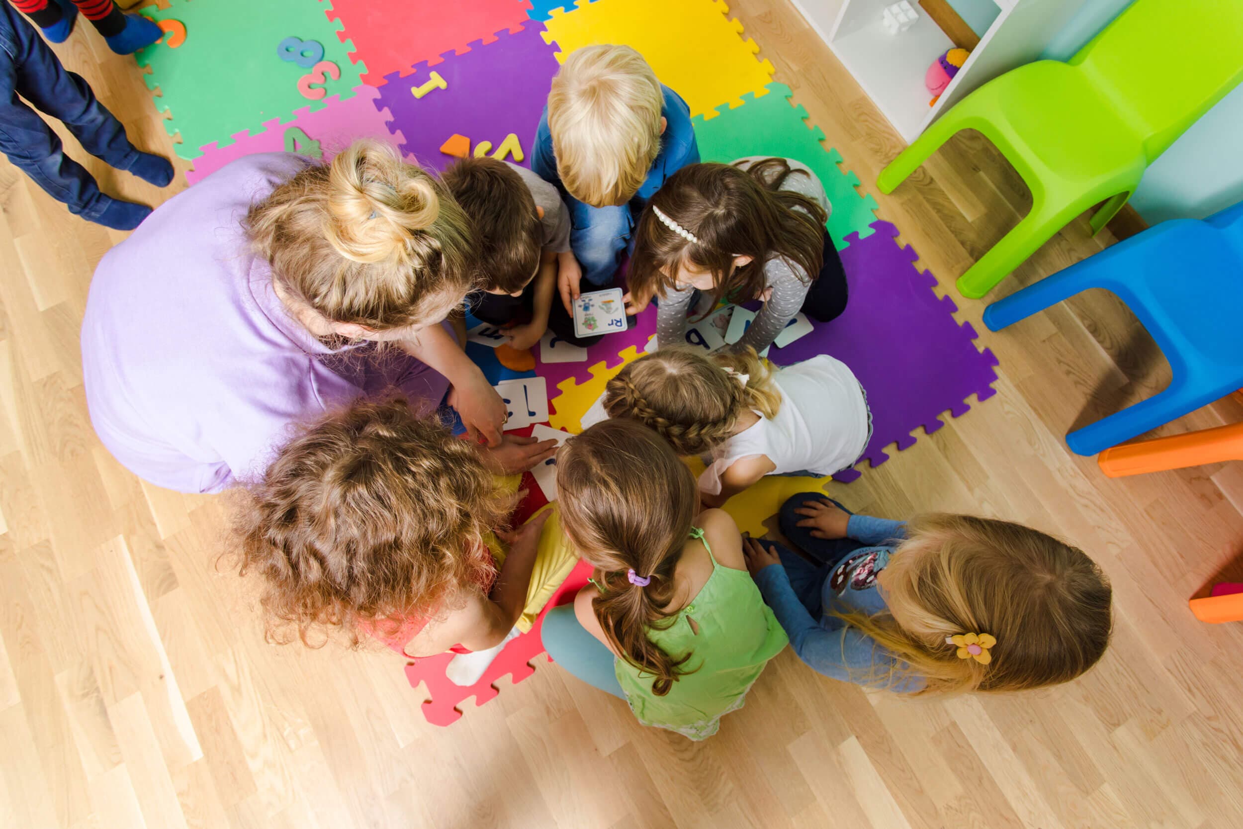 Children gathered in a circle on a foam play mat, seen from above