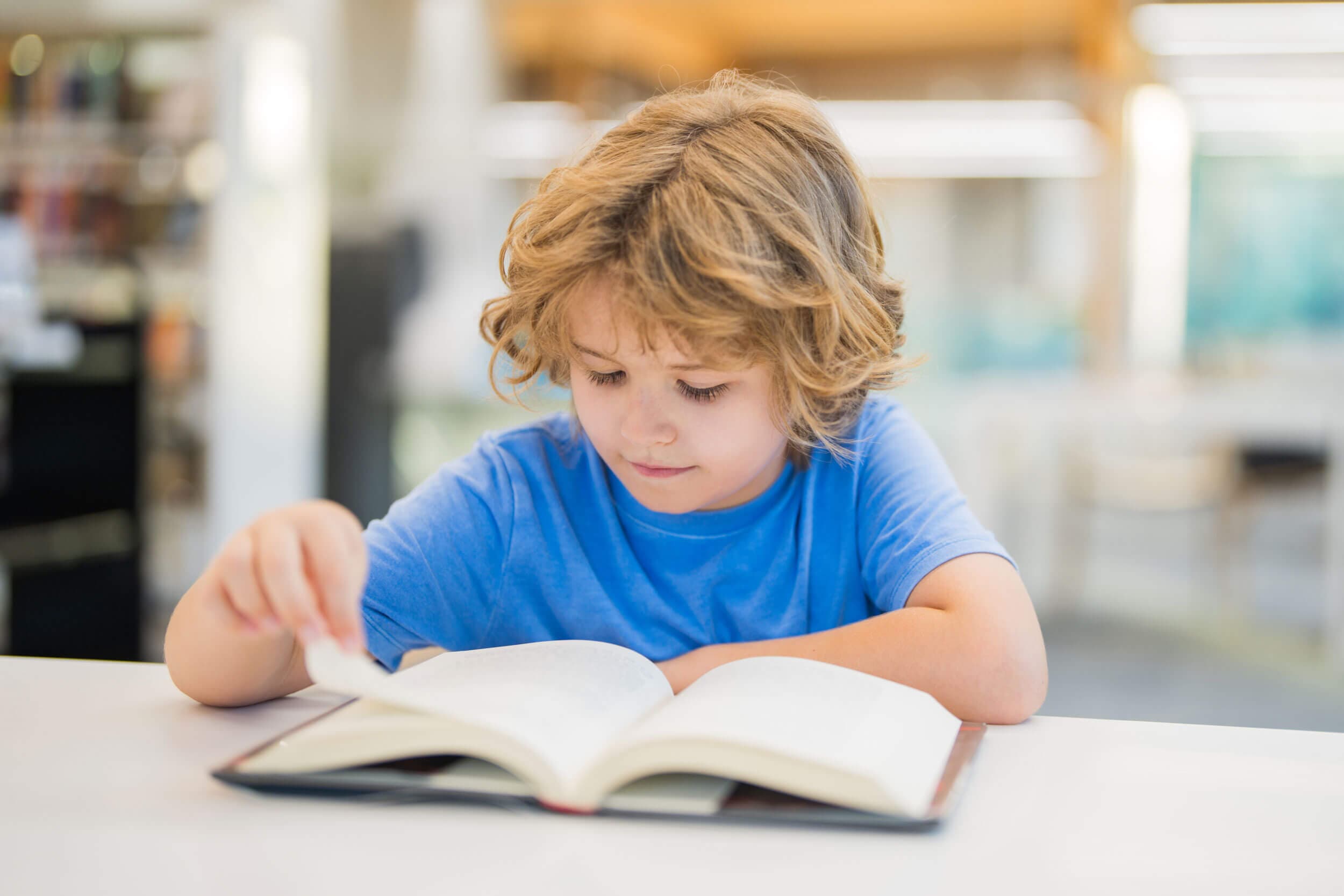A boy in a blue t-shirt turning the page of a large book