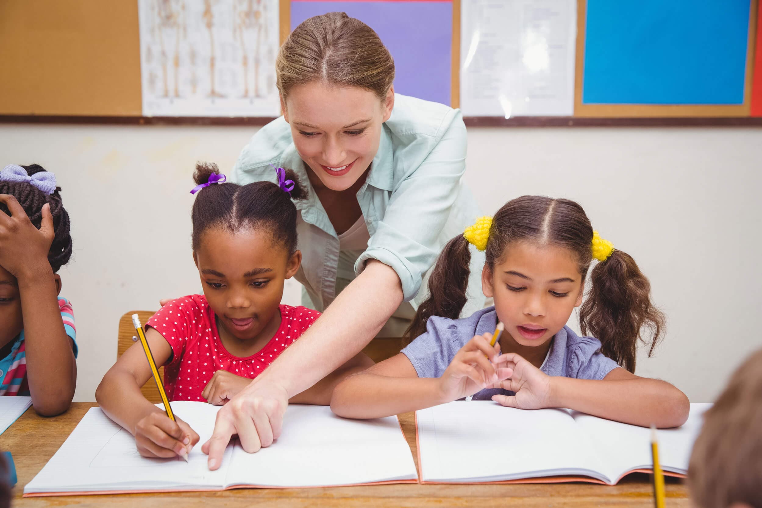 A teacher leaning in to help two girls writing at their desks