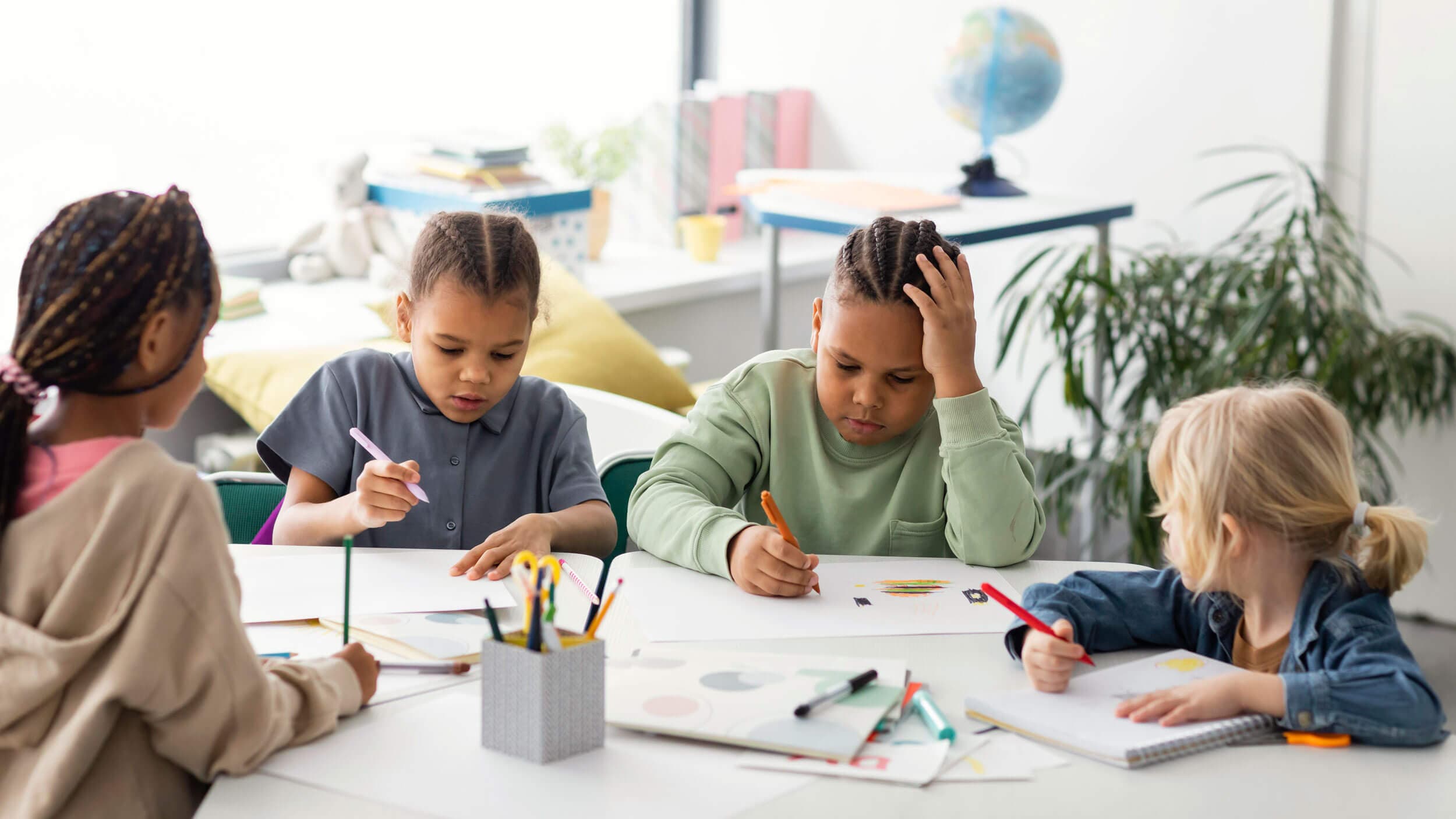 Four school-age children drawing independently at a shared classroom table