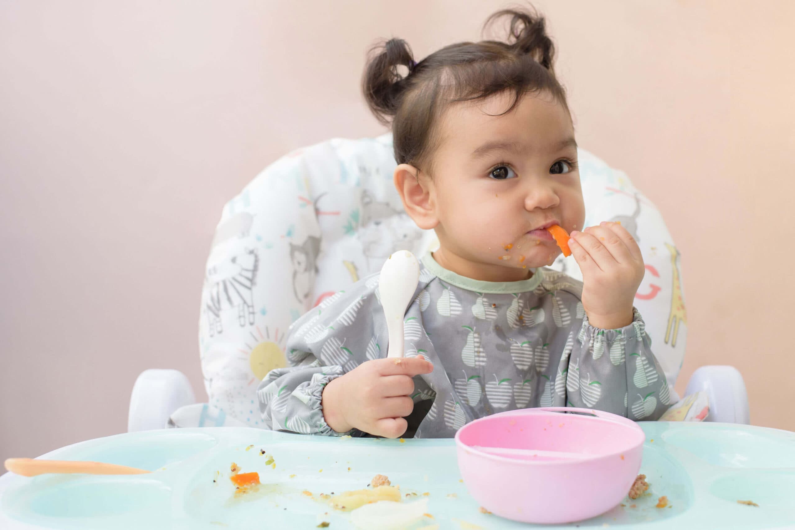 A baby in a highchair feeding themselves with a spoon