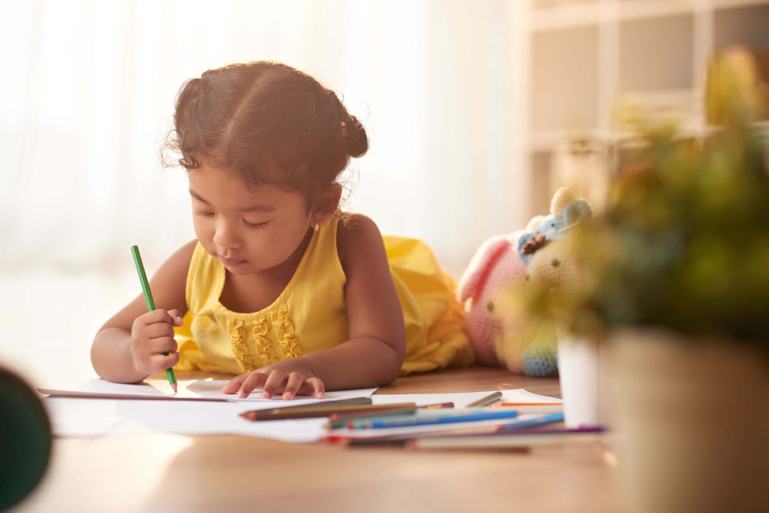 A girl in a yellow dress carefully drawing with a green pencil