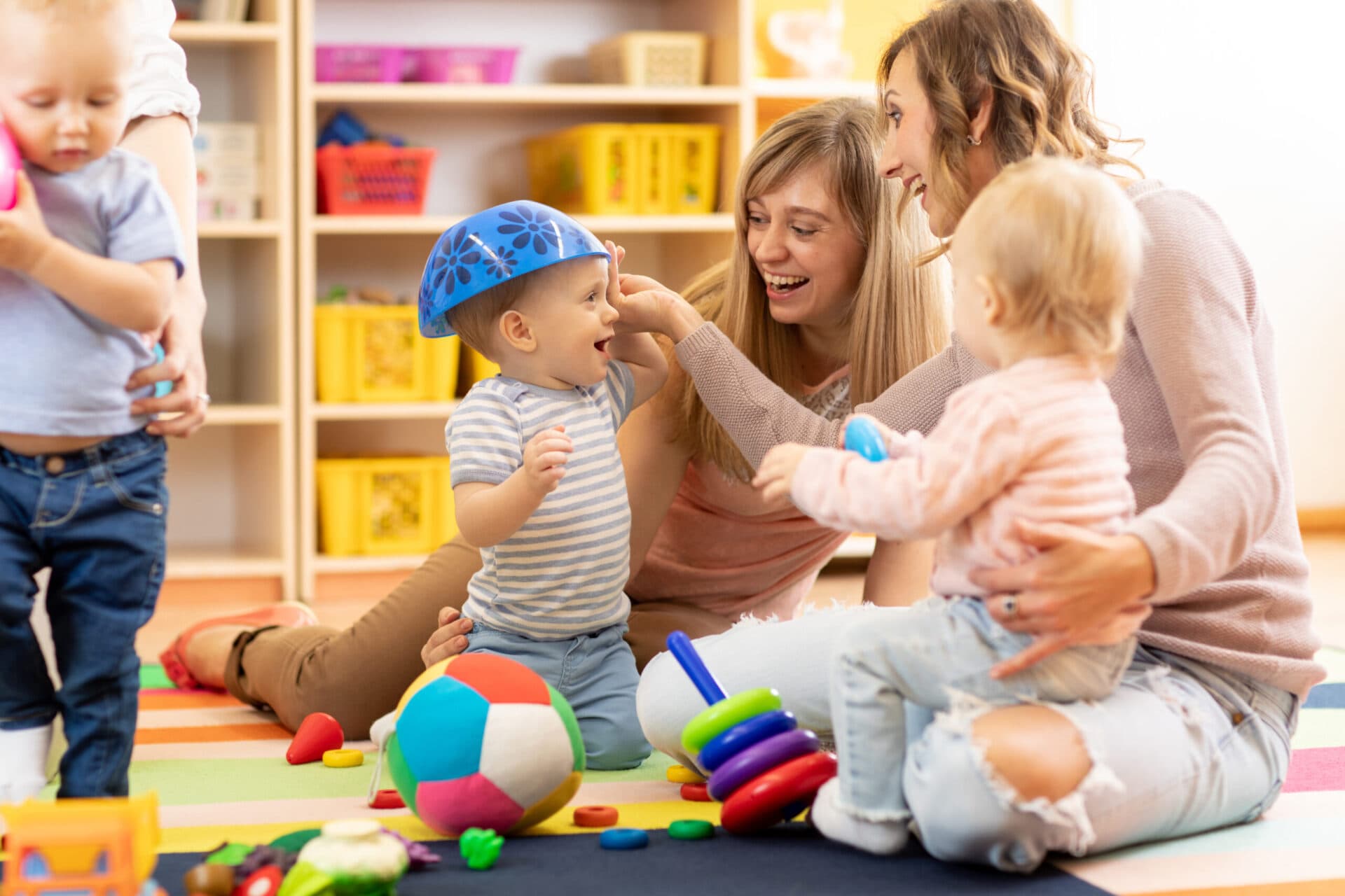 A teacher playing on the floor with two toddlers among soft balls and toys