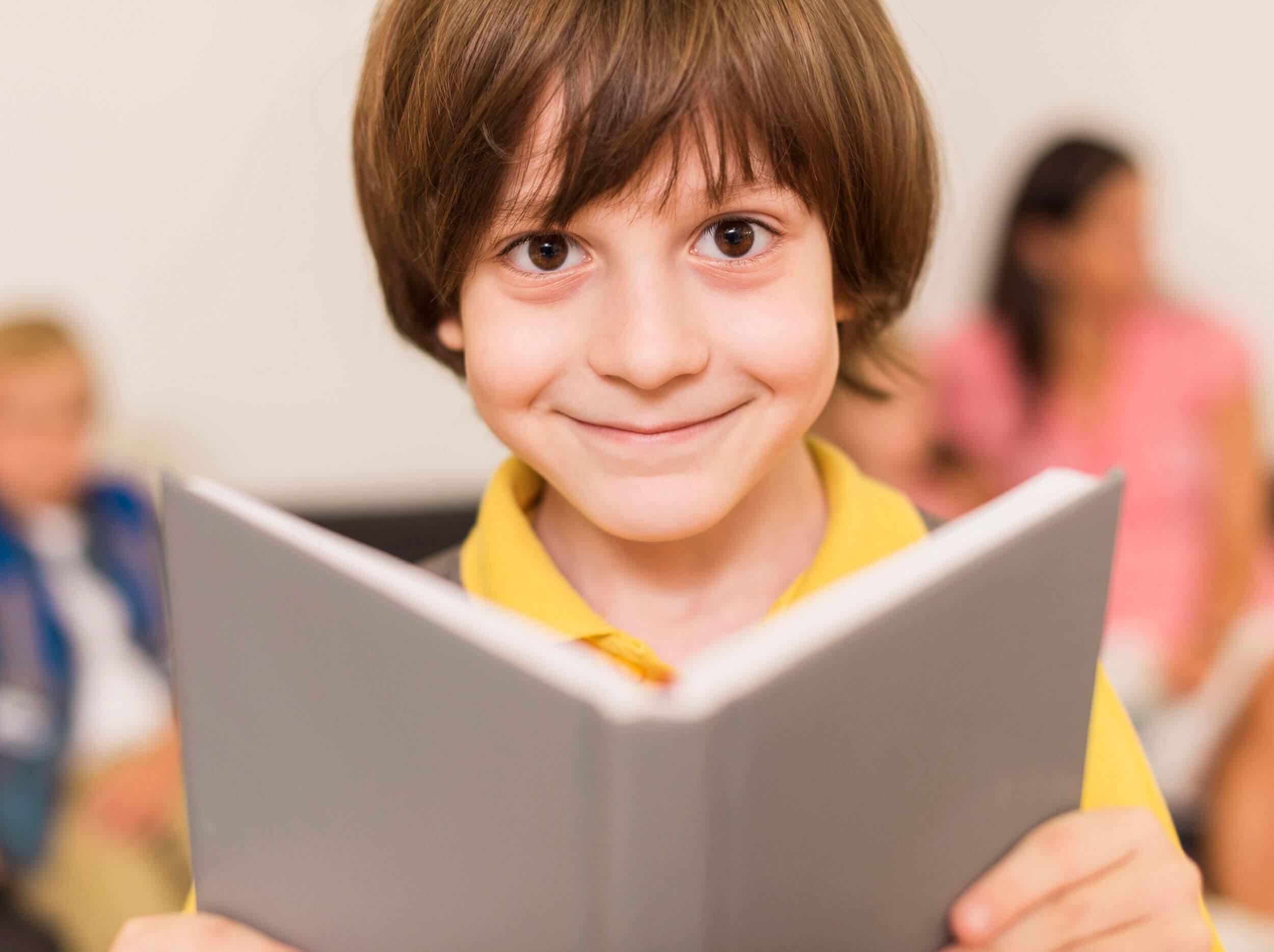 A boy smiling over the top of an open book