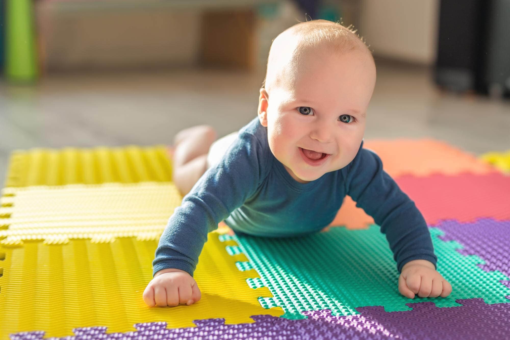 A baby in a blue top crawling across a foam play mat