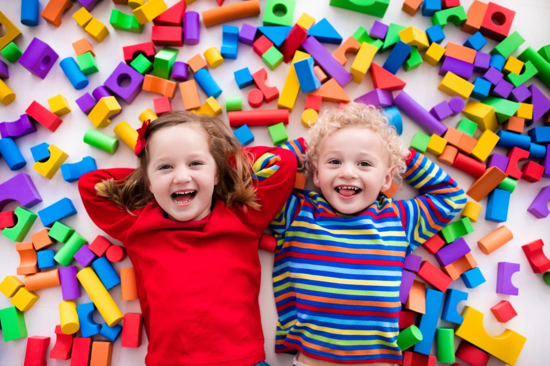 Two children lying among scattered building blocks, laughing at the camera