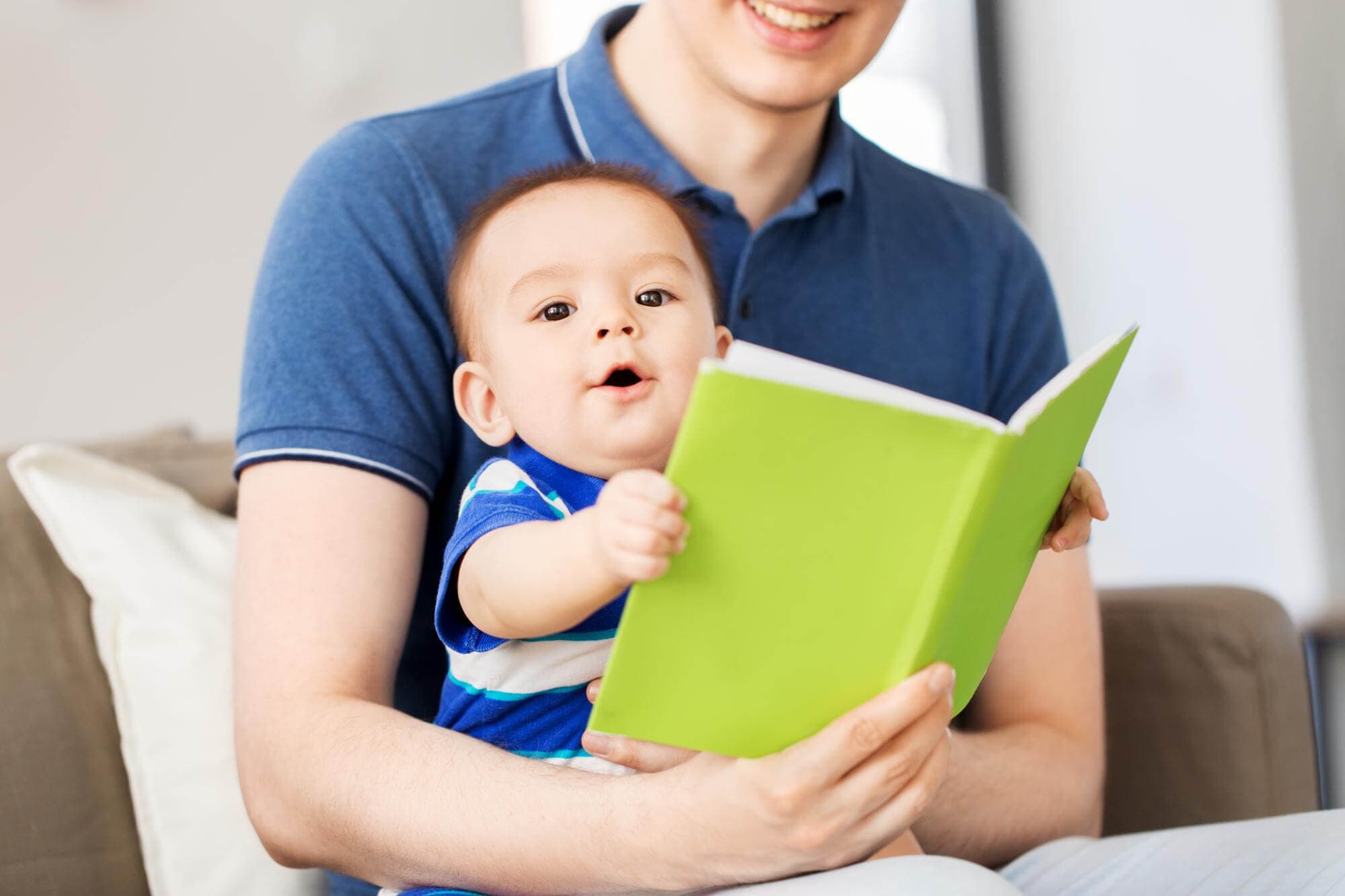 An adult holding a baby who is reaching for a bright green board book