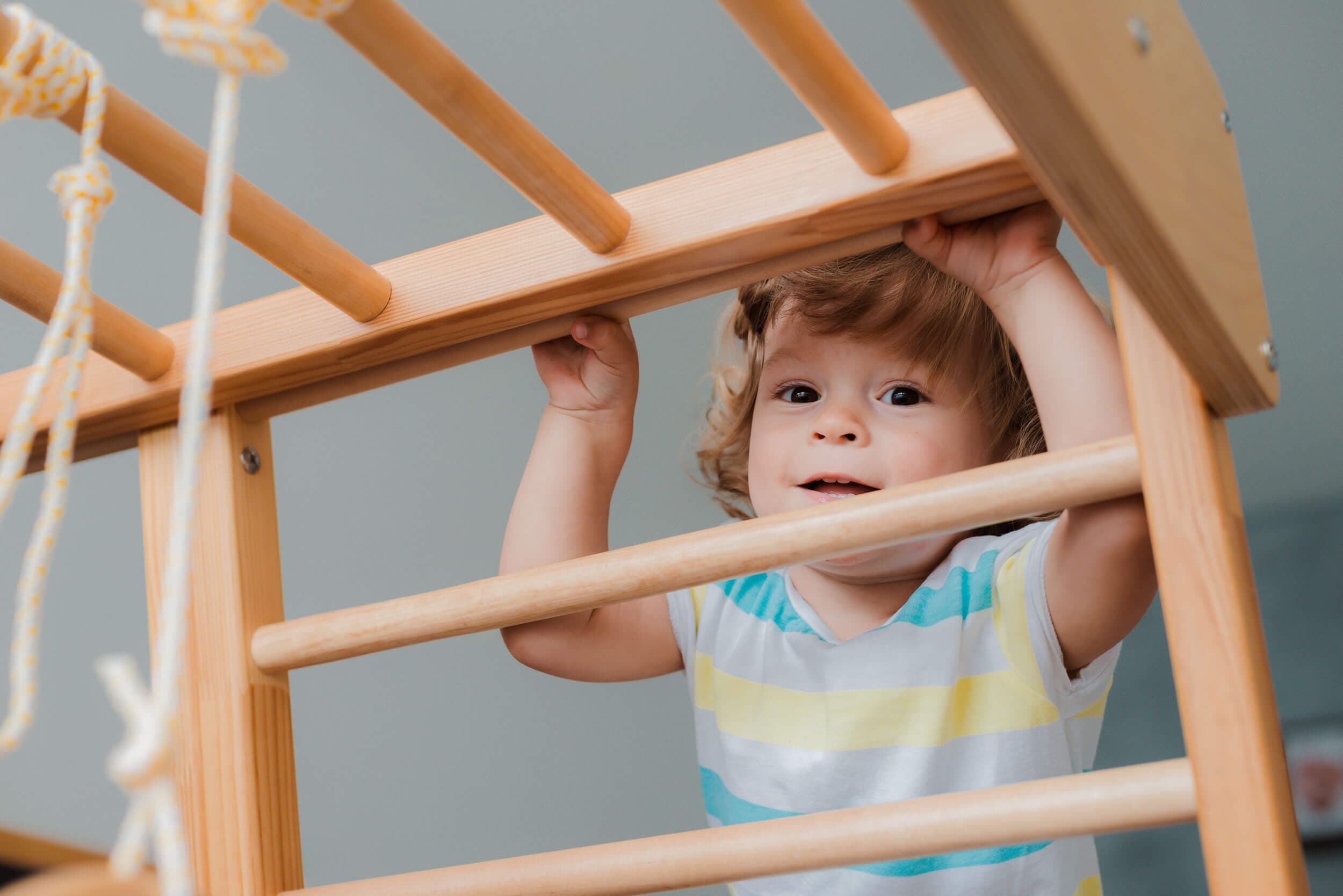 A toddler gripping the rungs of a wooden climbing frame