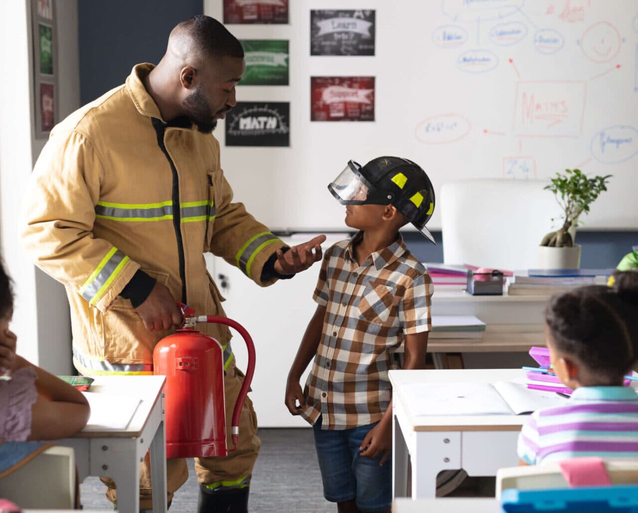 A firefighter showing his helmet and equipment to a child in the classroom