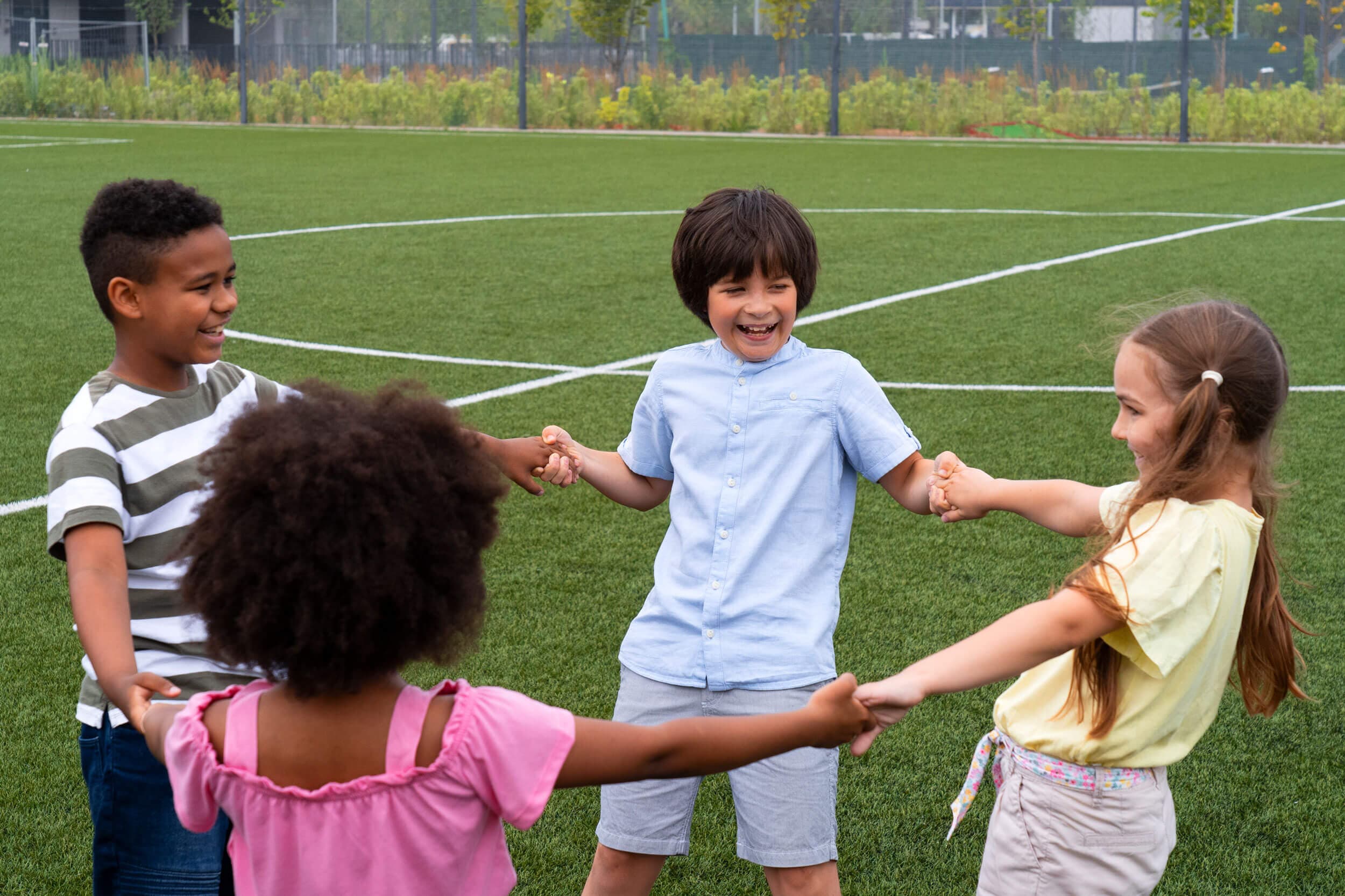 Four children holding hands in a circle on a grass field