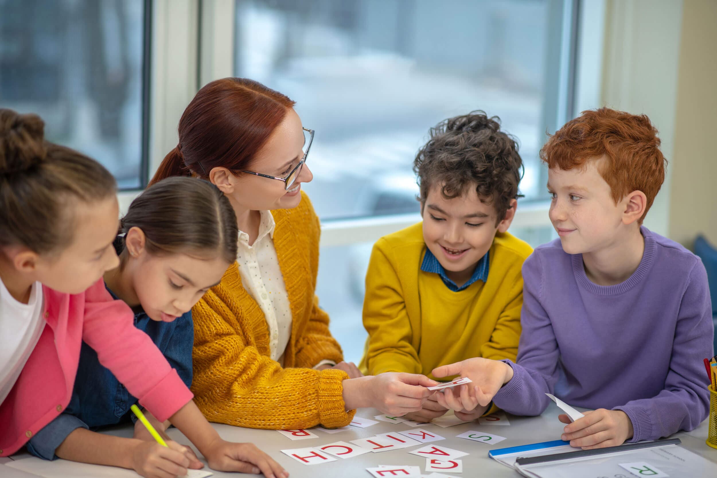 A teacher and four children looking closely at a card together at a table